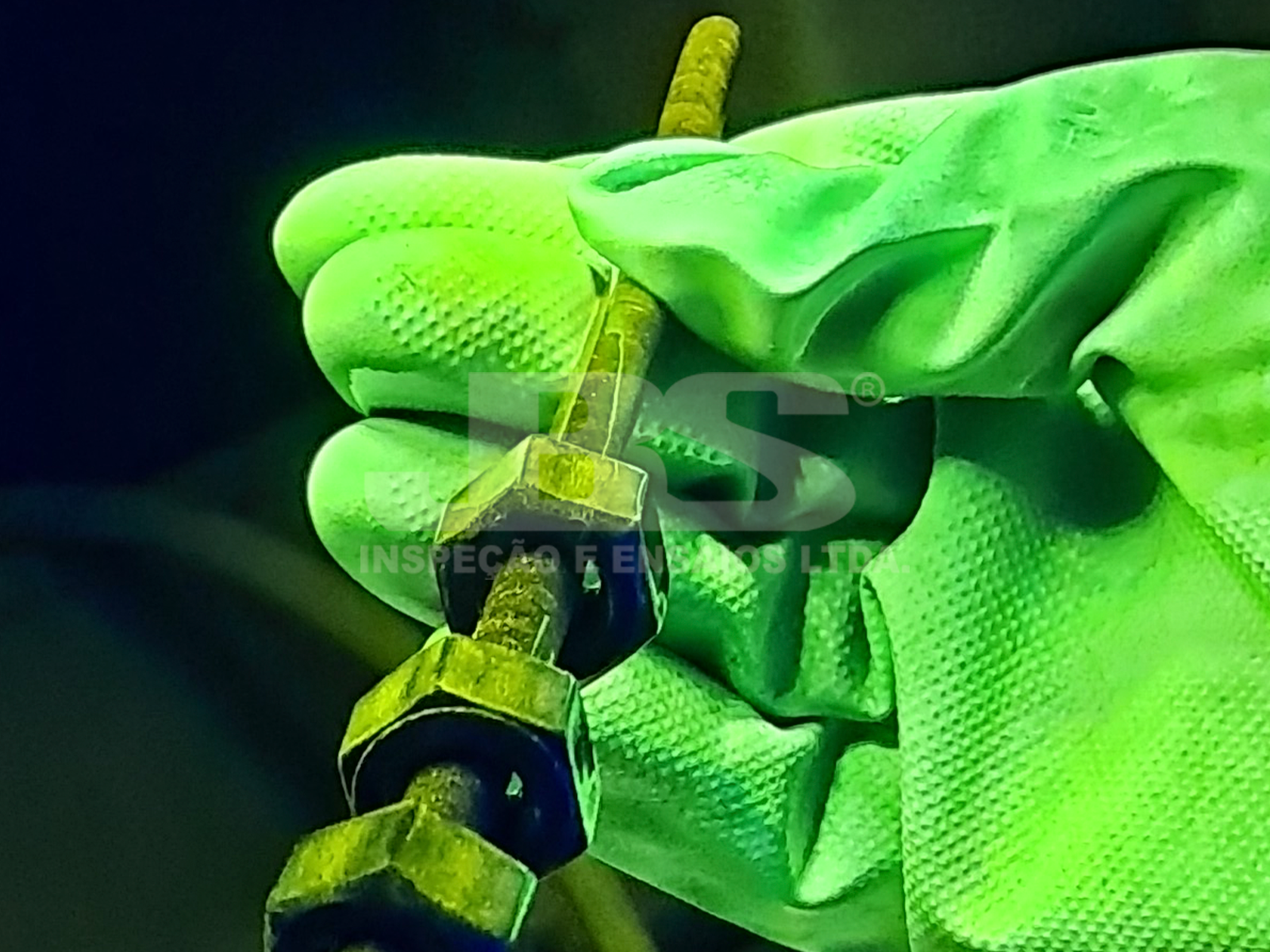 Inspetor com luva de proteção segura fixador após END (Ensaio Não Destrutivo). Inspecionado com partículas magnéticas, evidenciando fissura.